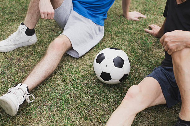 Legs of two generation football players resting on green grass.