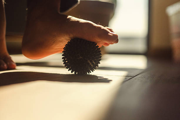 Close-up of a person massaging their foot with a spiky ball, promoting relaxation and wellness. The sunlight enhances the ambient and natural appeal of this reflexology or therapeutic technique.
