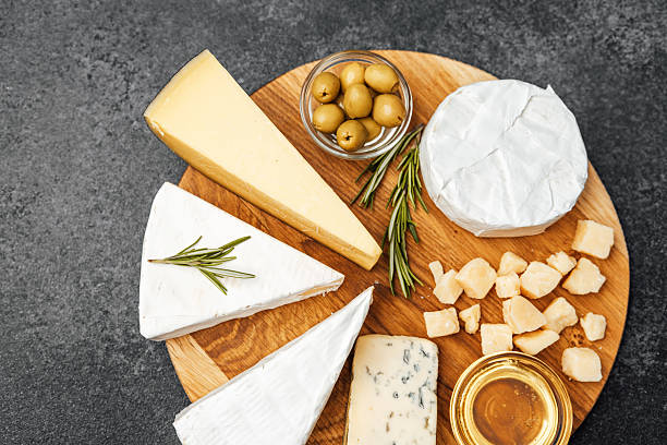 Varied cheeses arranged on a wooden board with bread slices and nuts, on transparent background, concept of gourmet food
