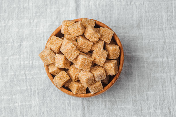istock Brown sugar cubes in a wooden bowl on a textured white surface 2215312701