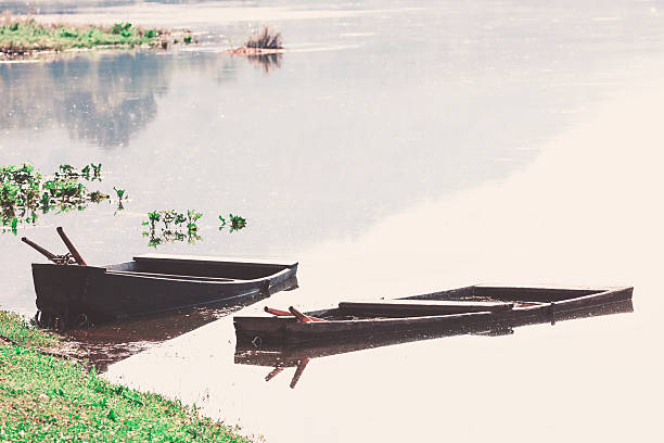 Tranquil scene of two boats on a river, showcasing the serene atmosphere. Wooden boats partially submerged in a calm body of water