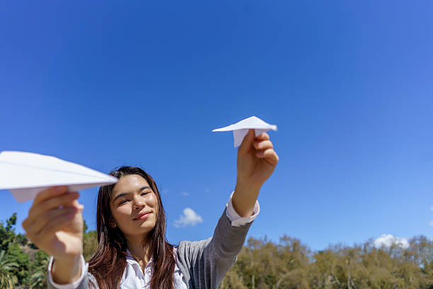 istock Young woman launching paper airplanes into a clear blue sky 2215342679