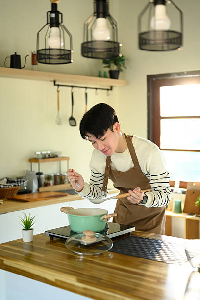 istock Young man smiling while preparing food in a home kitchen, standing over a pot on the stove 2215351741