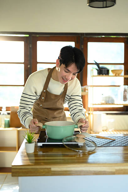 istock Young man smiling while preparing food in a home kitchen, standing over a pot on the stove 2215351754