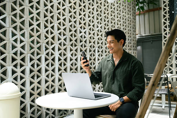 Smiling man having video call while working remotely on laptop at an outdoor urban cafe stock photo