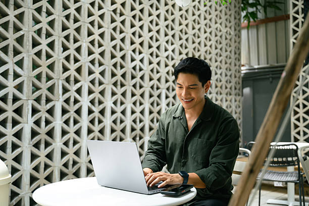 Smiling adult businessman working on his laptop at an outdoor cafe in the city stock photo