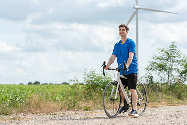 istock Caucasian man taking a break while riding bicycle at wind turbine field. Attractive athlete in sportswear exercise by cycling workout outdoors for health and wellness in rural area at windmill farm. 2215356614