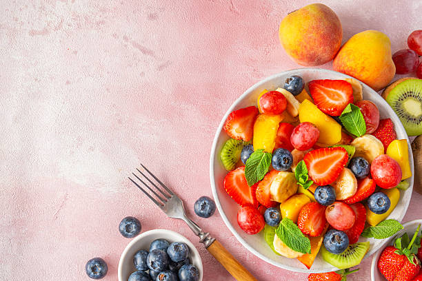 istock Summer colorful fruit salad in a bowl with fork on pink background. Top view with copy space. Healthy vitamin food for breakfast. Mixed strawberries, grapes, banana, kiwi, blueberries, peach, mint 2215358453