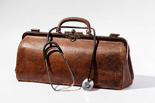 Vintage doctor bag and stethoscope resting on white background Old brown leather doctor bag with stethoscope on white background, representing healthcare and medical history leather medical bag stock pictures, royalty-free photos & images