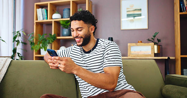 istock Phone, networking and man on sofa in home with typing for social connection on mobile app. Happy, relax and male person with cellphone for texting on media with online dating in living room at house 2215363224
