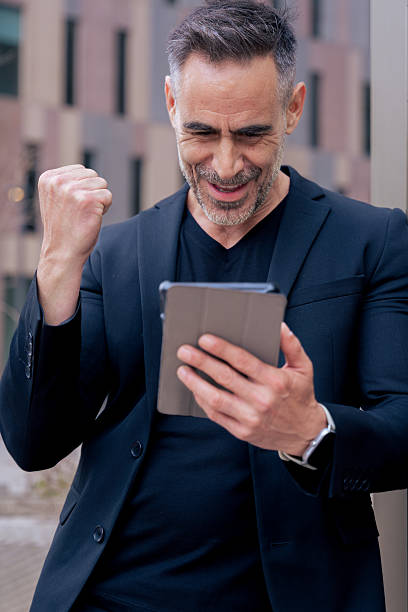 istock Excited mature man celebrating success while looking at tablet in city.Vertical 2215364539