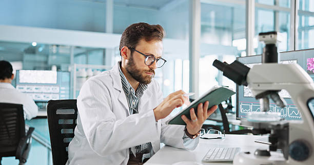 istock Scientist, man and tablet for study at laboratory with feedback, review and medical notes for pharma job. Person, typing and equipment with application for vaccine, development and clinical trial 2215368611
