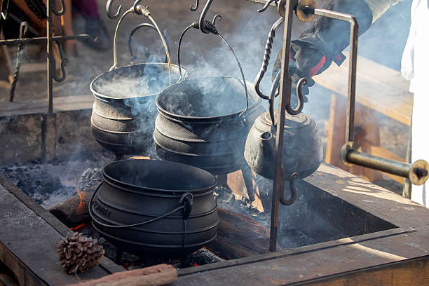 istock Traditional cast iron pots and kettle hanging over an open fire pit with rising smoke at outdoor historical camp. 2215371247