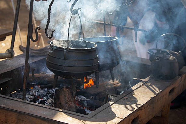 istock Traditional cast iron pots and kettle hanging over an open fire pit with rising smoke at outdoor historical camp. 2215371252