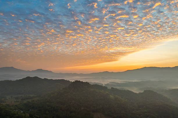 Aerial view of sunrise over misty mountain landscape with dramatic cloud formations, capturing the serene and golden beauty of a peaceful tropical morning.