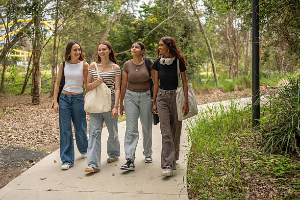 A group of four teenage girls walk side by side on a branching garden path surrounded by lush greenery and tropical plants in the quiet morning.