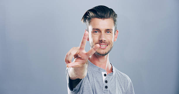 istock Portrait, space and happy man with peace sign, confidence or positive attitude for expression. Grey background, casual student and proud male model in studio for cool gesture, fashion or v symbol 2215380714