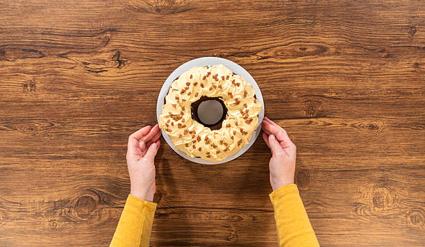 Flat lay. Carefully placing the gingerbread bundt cake, adorned with salted caramel frosting and gingerbread sprinkles, into a white paper bundt cake box with a clear window for gifting.