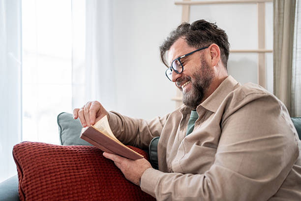 istock Mature man reading a book and smiling on the sofa 2215392552