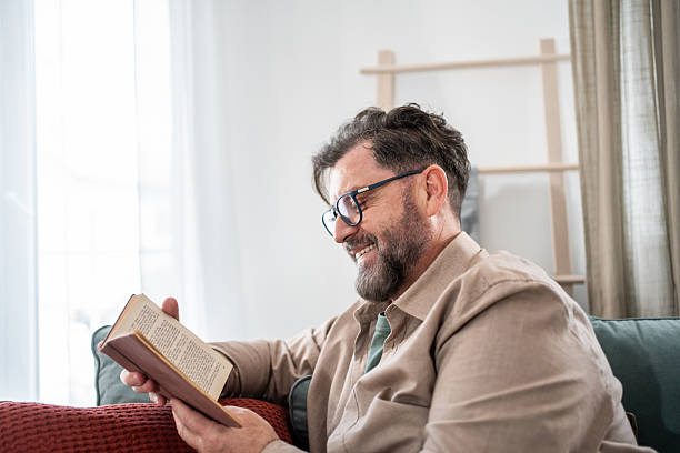 istock Smiling mature man reading a book at home on the sofa 2215392675