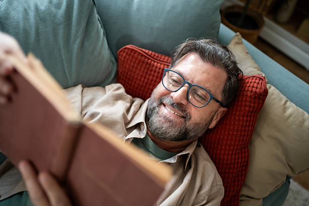 istock Happy mature man reading a book at home smiling 2215393372