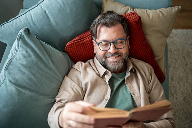 istock Mature man relaxing on sofa reading a book and smiling 2215393375