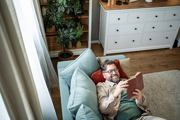 istock Mid adult man relaxing on sofa reading a book at home 2215393380
