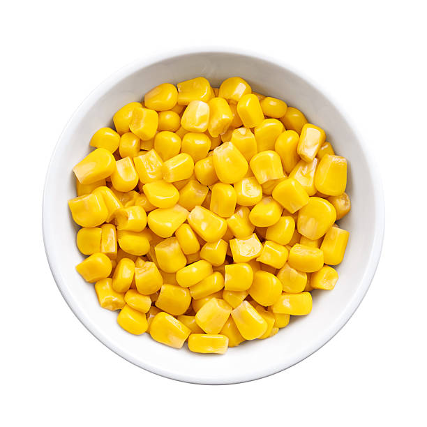 Canned corn, vegetable maize, whole sweet corn kernels in a white bowl. Variety of corn that is picked when in its milk state. Fully cooked kernels, preserved and ready to eat. Isolated, from above.