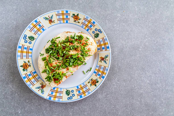 A slice of buttered bread with fresh chives is served on a checkered plate, placed on a gray countertop. The scene captures a simple and cozy kitchen moment with natural textures.