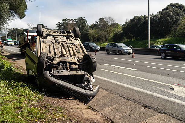 Damaged wrecked car after collision lying upside down on roadside. Busy city street with car rolled over during daytime. Car accident