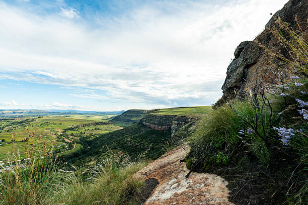 : Beautiful valleys with greenery and farmland stretch across the horizon, viewed from a mountain's edge