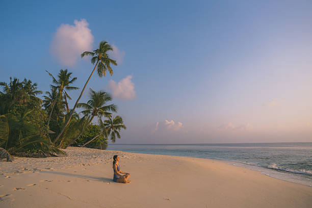 istock Young woman meditates on beach at sunrise 2215411505