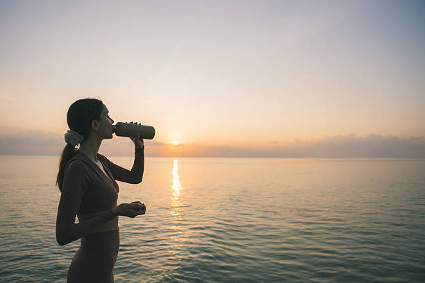 istock Young woman drinks from water bottle as sun rises over tropical lagoon 2215411562