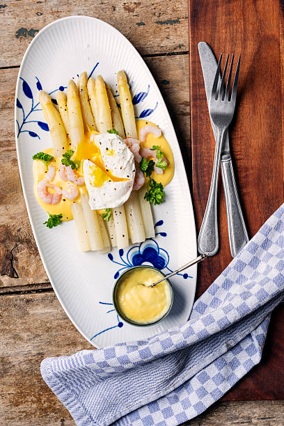 Overhead view of a dish of white asparagus served with a poached egg, prawns, and a hollandaise sauce.