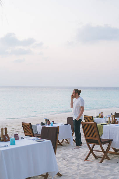 istock Young man talks on phone at beach restaurant at sunset 2215414266