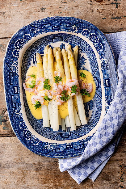 Overhead view of a dish of white asparagus served with prawns and a hollandaise sauce.