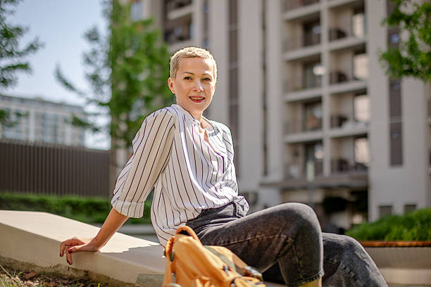 istock Young woman with short hair smiles joyfully while sitting outdoors in a modern urban setting during the day 2215414836