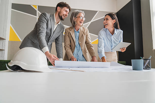 istock Team of multiethnic architects working on construction plans in meeting room. Engineers discussing on project in office. Businesswoman and her colleagues standing around table working on blueprint. 2215418639