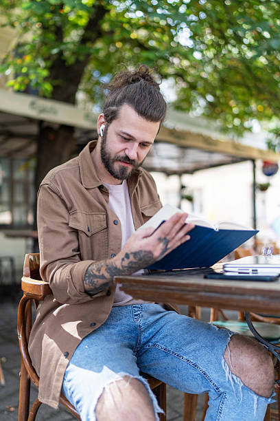 istock Young man reading a book at an outdoor cafe 2215420158