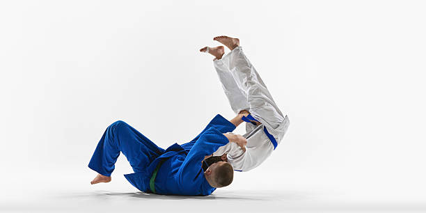 istock Judoka in blue brings white gi opponent crashing down using classic seated throw technique against white background. 2215421577