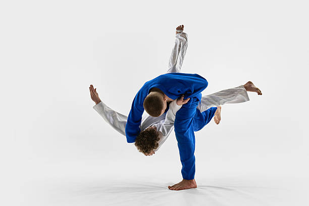 istock Blue gi fighter thrown over shoulder in fast motion by white gi athlete against white studio background. Concept of judo, combat sport 2215421583