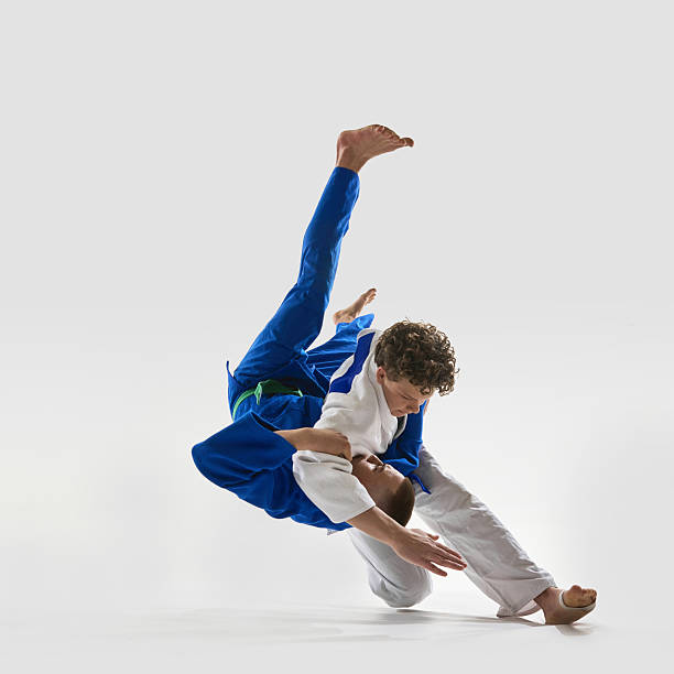 istock Flawless takedown in motion, fighter in white executing classic over-the-shoulder throw as blue gi opponent is launched into air, highlighting mastery against white background. 2215421589