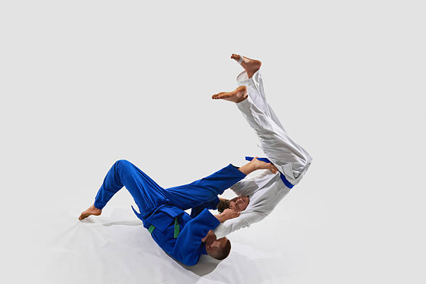 istock Fighter in blue launches opponent using leg-assisted takedown, body lifting mid-rotation, symbolizing power against white background. 2215421594