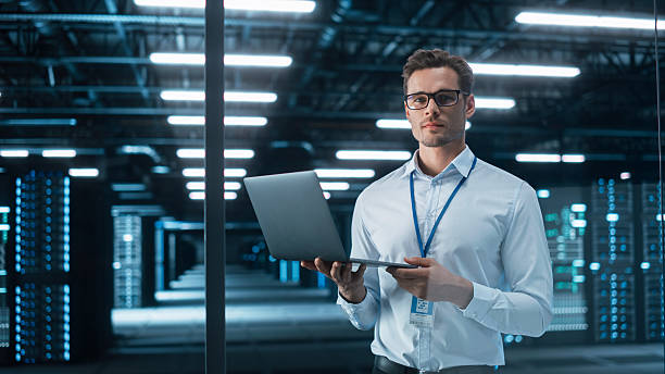 istock Creative Businessman Standing in Modern Office, Hold Laptop Computer and Look at the Camera. Successful Managing Director Planning Work Projects at the Evening Working Room 2215422796