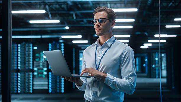 istock European Male IT Specialist Using Laptop Computer, Standing in Big Warehouse Data Center. System Administrator working with SAAS. E-Business Digital Entrepreneur Examining Cloud Web Services 2215422861