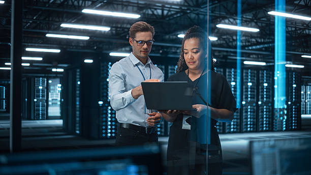 istock Diverse Big Data Center Server: Entrepreneur and IT Specialist Look at Laptop Screen and Talk. Information Technology Engineer and System Administrator Monitoring Web Services Cloud Solution Software 2215423234