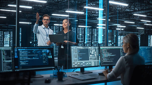 istock Multiethnic Female System Administrator and Caucasian Male Information Technology Engineer Discussing and Brainstorming with Laptop while Work in Tech Facility Data Center 2215423306
