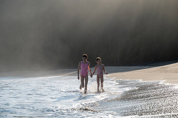 Young girls running along beach at sunrise, Mokuleia Beach, Maui