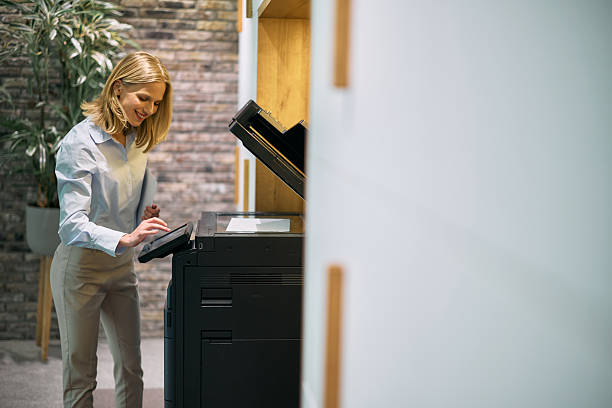 Smiling businesswoman interacting with the touchscreen of a modern multifunction printer in the office, efficiently making photocopies and scanning important documents