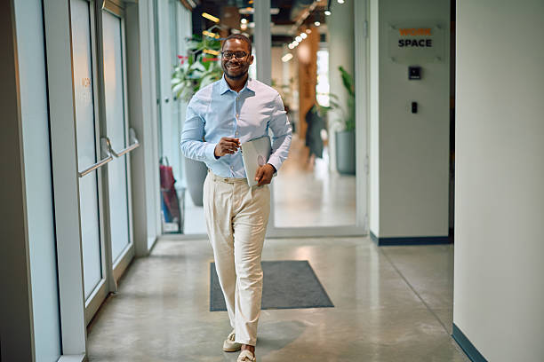 istock Confident businessman walking through modern office hallway carrying laptop 2215425636